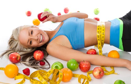 Kvinde med målebånd rundt om maven omgivet af frugter